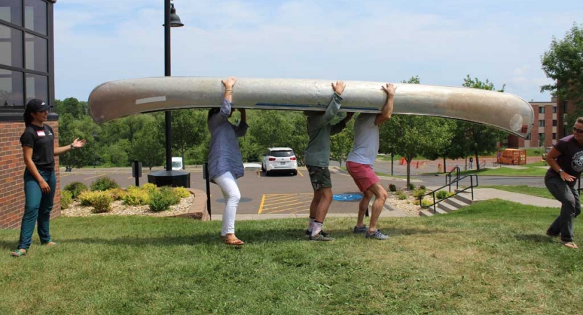 Three people carry an upside-down canoe on their shoulders at the family seminar of an outward bound intercept course